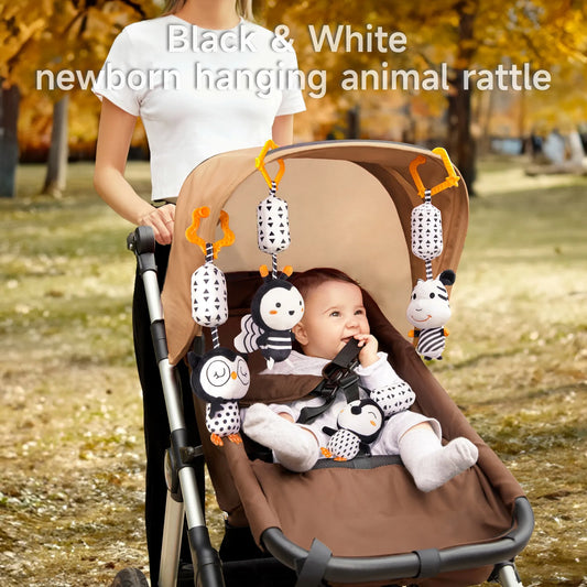 A baby is sitting in a stroller, looking at the black and white animal hanging toy