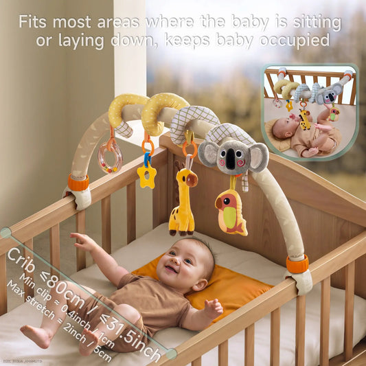 A baby lying on a bed looking at a stroller arch toy