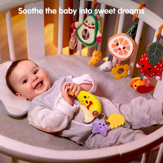 Baby lying in bed looking at baby toys hanging fruit rattles