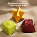 Three colorful textured sensory blocks—a yellow star, a green cube, and a red square pyramid—are displayed on a soft beige fabric surface. Each toy features rounded edges and tactile patterns designed for safe play. The text “Rough edge design and safe for your baby” appears at the top, highlighting their baby-safe construction.
