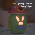 Nighttime view of a mushroom-shaped baby toy glowing with soft, warm light through a bunny-shaped design. The gentle illumination is designed to protect baby's eyes, making it suitable for bedtime use as a comforting nightlight.