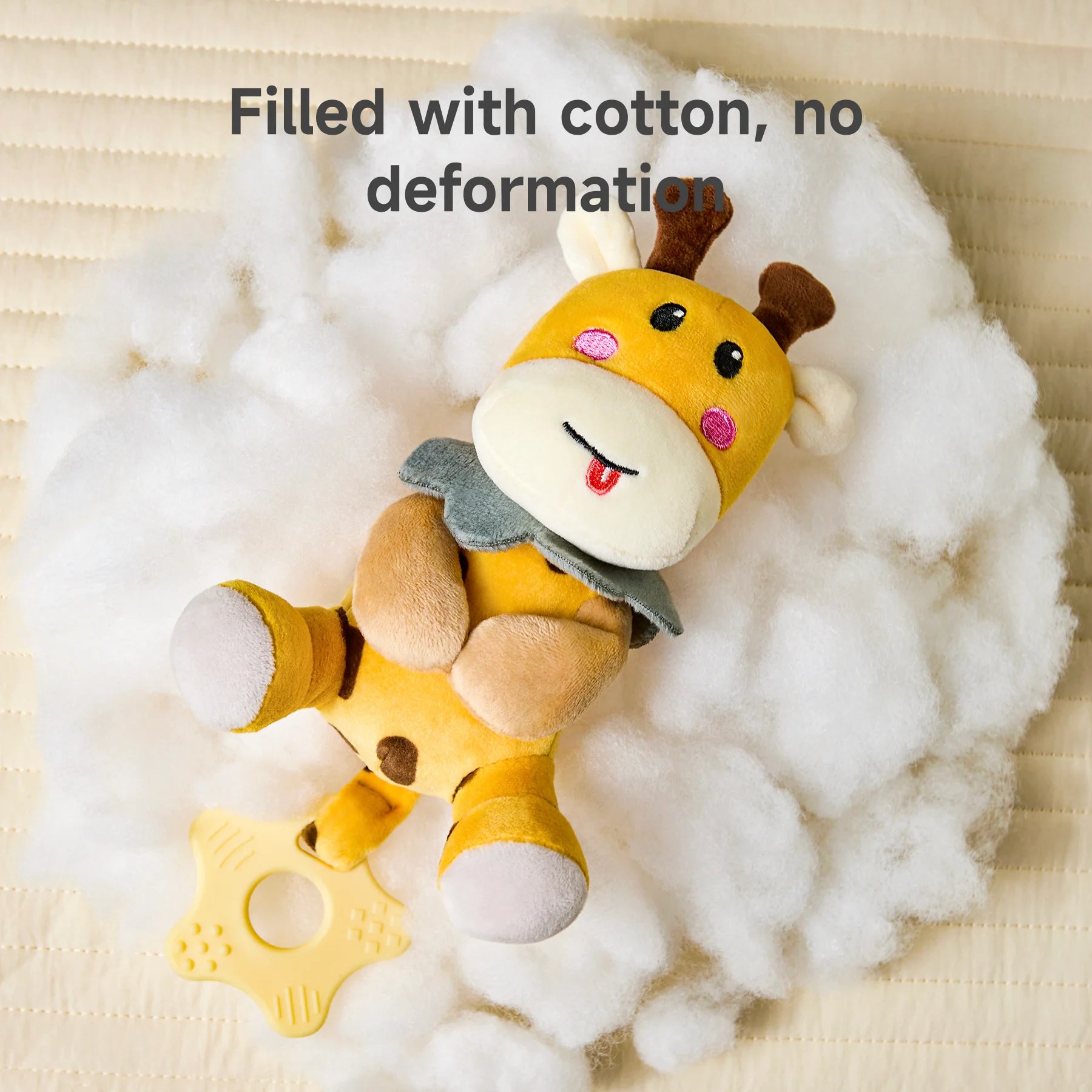 Plush giraffe rattle toy with a star-shaped teether handle, lying on fluffy white cotton filling. The text reads: “Filled with cotton, no deformation.”