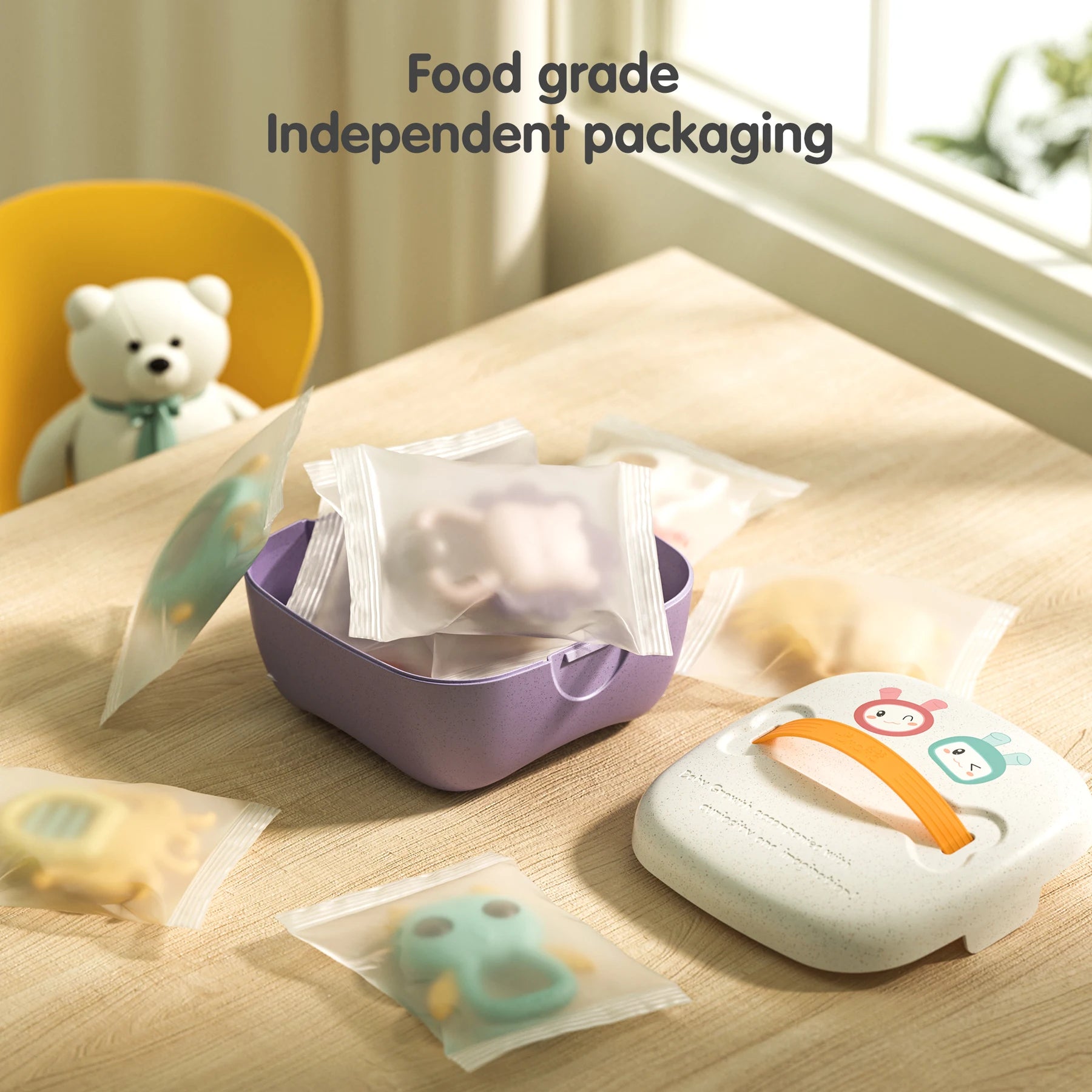Baby teethers individually sealed in clear, food-grade plastic bags, shown on a wooden table next to an open purple container and its white lid with cartoon faces and an orange handle. Text on the image reads “Food grade Independent packaging,” emphasizing hygiene and safety in product storage.