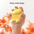 Hand holding a yellow frog-shaped baby teether toy with water droplets on its surface and water draining from a small outlet at the bottom. The background features soft orange flowers, and the text reads “Water outlet design,” highlighting the toy’s easy-to-drain feature for cleaning or water play.