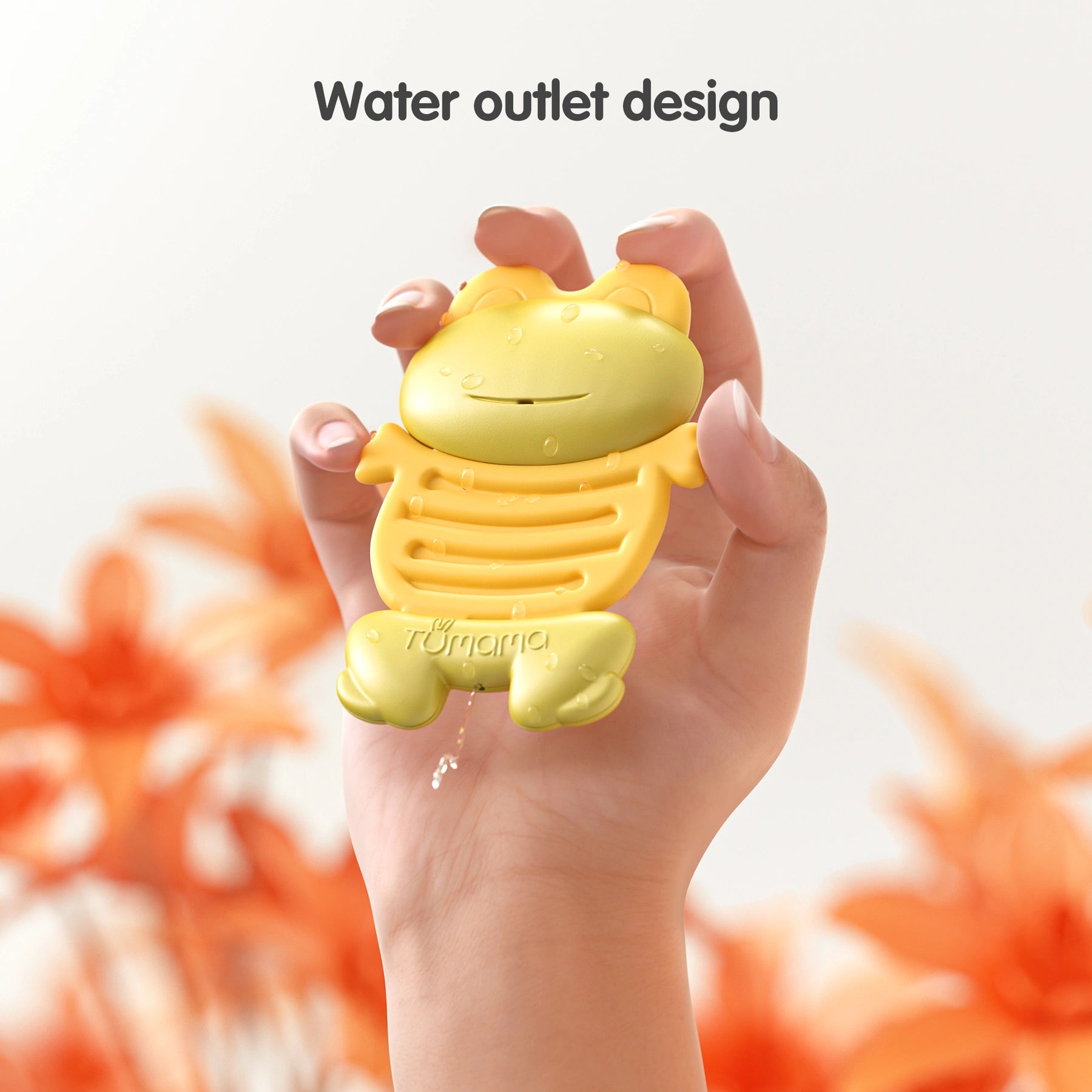 Hand holding a yellow frog-shaped baby teether toy with water droplets on its surface and water draining from a small outlet at the bottom. The background features soft orange flowers, and the text reads “Water outlet design,” highlighting the toy’s easy-to-drain feature for cleaning or water play.