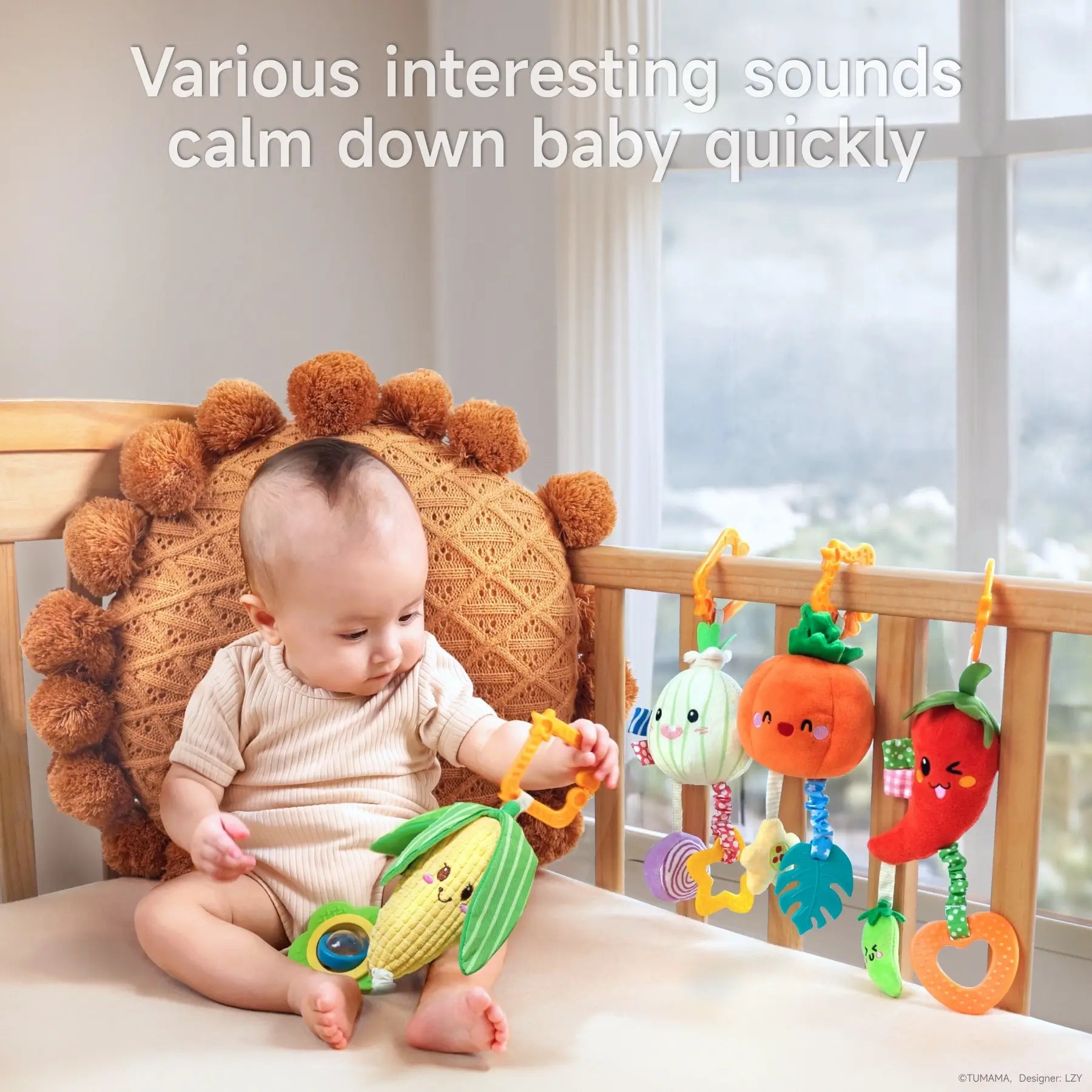 Baby sitting on a bed playing with a plush corn rattle while additional hanging vegetable toys—onion, pumpkin, and chili pepper—are attached to the crib, providing calming sounds to soothe the baby.