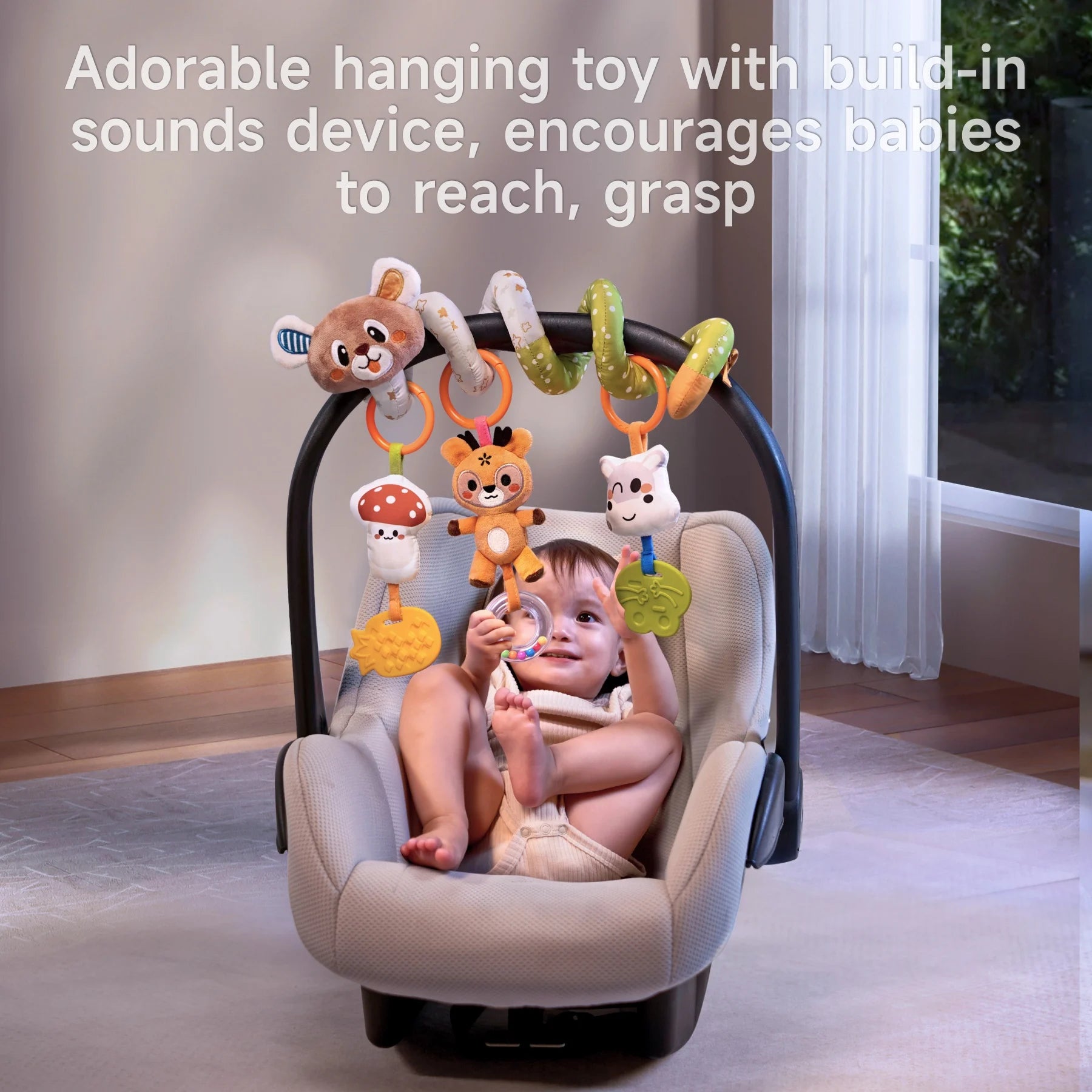 Smiling baby in a car seat reaching up to play with a colorful hanging toy arch featuring plush animals and shapes, each with a built-in sound device to stimulate sensory development and encourage grasping.
