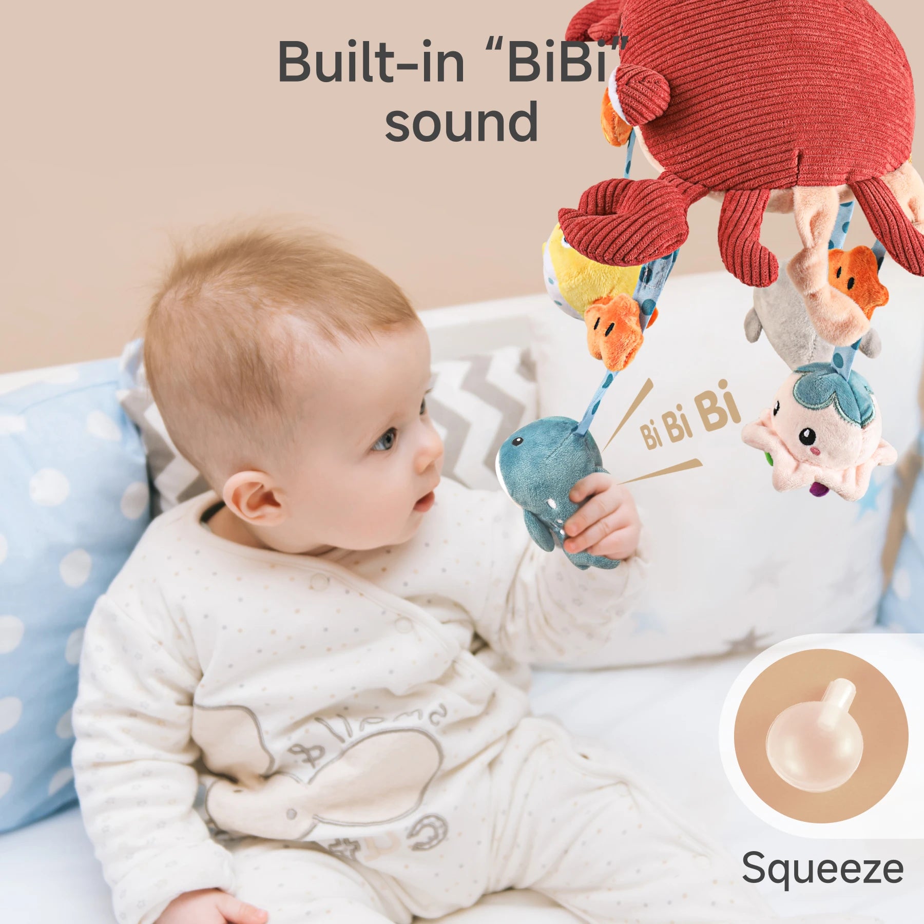 A baby sits comfortably while wearing a cream-colored onesie adorned with a subtle pattern. The infant is engaged with a playful plush toy fashioned like a crab. This toy features a blue hanging element accented by a red band around its arms and appears to offer an interactive feature that activates a sound when squeezed.