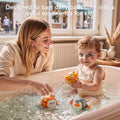 A happy toddler sits in a bathtub playing with colorful wind-up swimming bath toys shaped like a duck, bunny, and penguin, while an mother, smiles and interacts with the child. Text above reads: “Designed to turn daily bath time into a joyful experience for kids.”