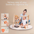 Mother and baby playing with black, white, and orange hanging plush toys under a wooden play gym. The baby explores soft toys featuring crinkly sounds, squeakers, and textured teethers. Soft cloth books are placed on the play mat. Text overlay reads: “Various way of play – Soothe & cognitive toy,” with close-up insets showing interactive toy features.