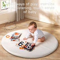 A baby sits on a round white mat in a sunlit room, engaging with black, white, and orange high-contrast soft cloth books featuring large numbers and patterns. The text above reads “Multi-ways of play, exercise visual, listening, touch sense of baby,” and a playful “sha sha~” sound bubble appears, indicating a crinkly sound feature for sensory stimulation.