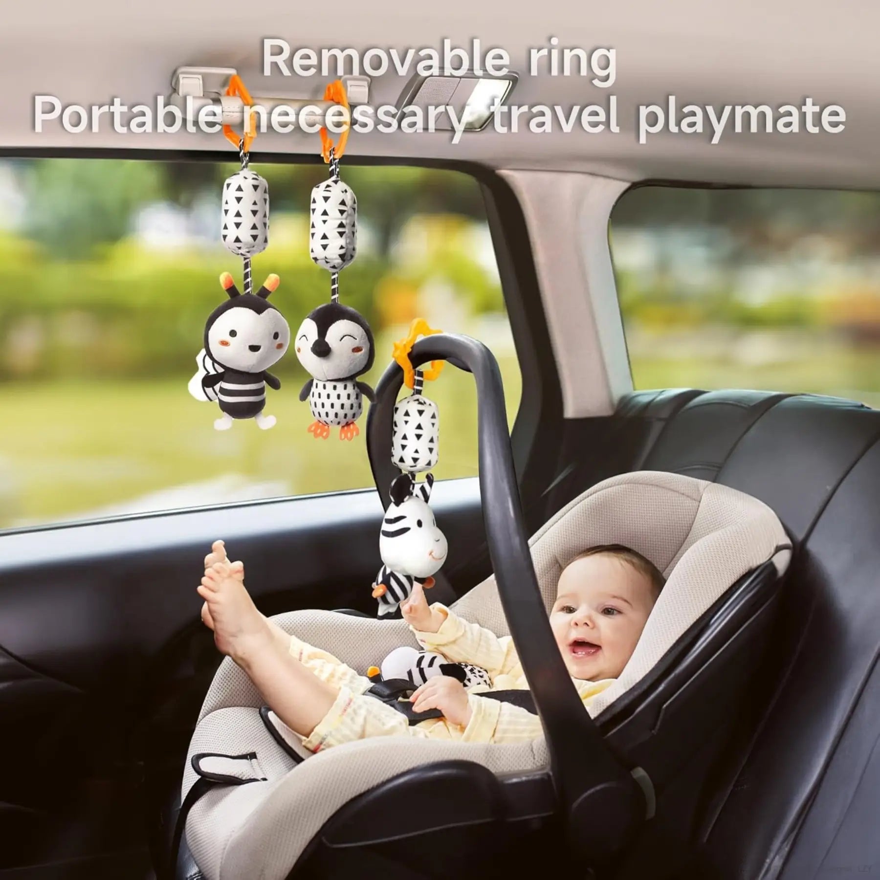 Smiling baby in a car seat playing with black and white hanging plush toys featuring animal designs, attached using removable rings to the car's handle and ceiling hook, illustrating their portability and use as ideal travel playmates.