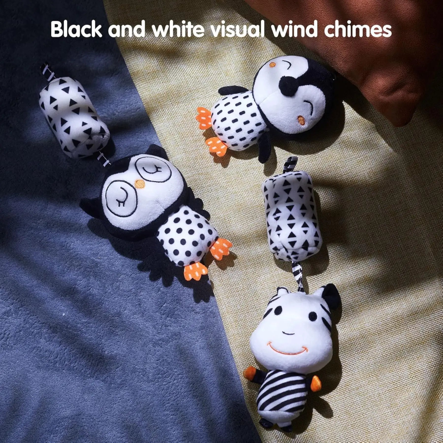 Three black and white baby plush wind chimes featuring owl, penguin, and zebra characters with high-contrast patterns designed to stimulate infant visual development, placed on a soft surface with natural light and shadow.