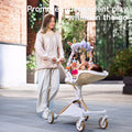 Mother pushing a stroller outdoors with a baby engaged in independent play, reaching for a colorful animal-themed hanging toy arch attached to the stroller.