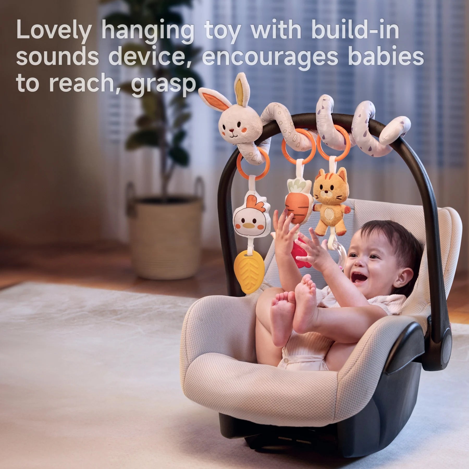 Smiling baby sitting in a car seat, joyfully reaching for plush animal and vegetable toys hanging from a soft arch with sound devices, promoting sensory interaction and grasping skills indoors.