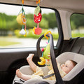 A baby seated in a car seat playing with colorful plush fruit-shaped hanging rattle toys attached to the car interior. The toys, including avocado, orange, and strawberry designs, feature soft textures and dangling accessories, keeping the baby entertained and stimulated during travel.