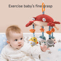 A baby is sitting in a crib, reaching out with curiosity to grab a plush hanging crab toy with dangling sea animal plushies (fish, whale, shark, and dolphin). The toy is suspended above, and the baby looks engaged and focused. The text above reads: “Exercise baby's fine grasp”.