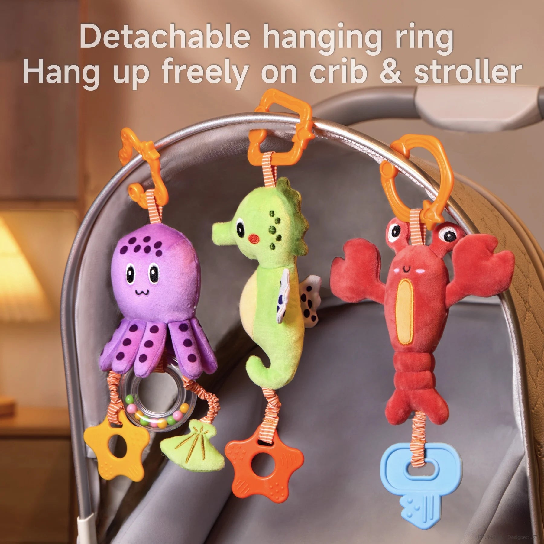 Three colorful marine-themed plush toys (an octopus, seahorse, and lobster) hanging on a stroller canopy using detachable orange plastic rings. Each toy includes sensory features like a rattle, teether, or crinkle parts. Text at the top reads: “Detachable hanging ring – Hang up freely on crib & stroller.” Soft indoor lighting creates a cozy setting.