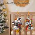 Two black and white high-contrast sensory cube toys hanging from a wooden crib rail. Each toy features colorful tags, teethers, rattles, and plush animal faces, designed to stimulate newborn vision and keep babies engaged. A Christmas tree with lights is visible in the background, creating a cozy nursery atmosphere.