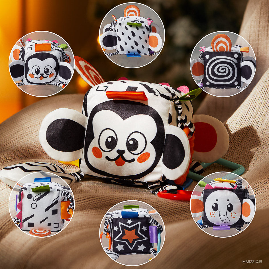 High-contrast baby sensory cube toy with multiple sides featuring black and white patterns, cute animal faces, stars, and spirals. The soft cube includes colorful tags, crinkle textures, and attached teethers to stimulate visual development and sensory exploration for infants.