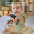 Baby chewing on a soft black-and-white crab-shaped sensory toy with orange claws and multiple teether attachments. The plush toy features high-contrast patterns, hanging rings, and rattles, designed to soothe teething discomfort while stimulating visual and tactile development.