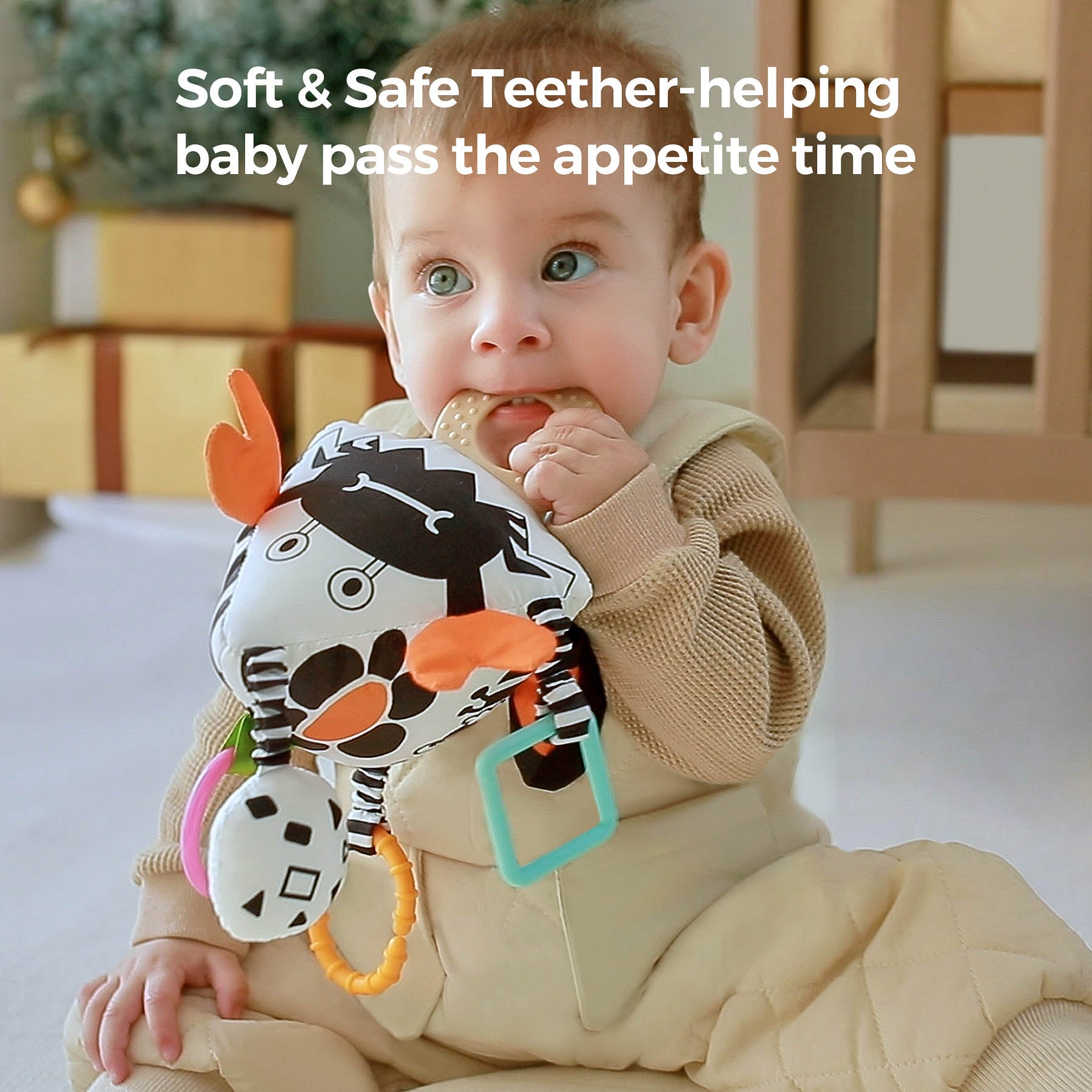 Baby chewing on a soft black-and-white crab-shaped sensory toy with orange claws and multiple teether attachments. The plush toy features high-contrast patterns, hanging rings, and rattles, designed to soothe teething discomfort while stimulating visual and tactile development.