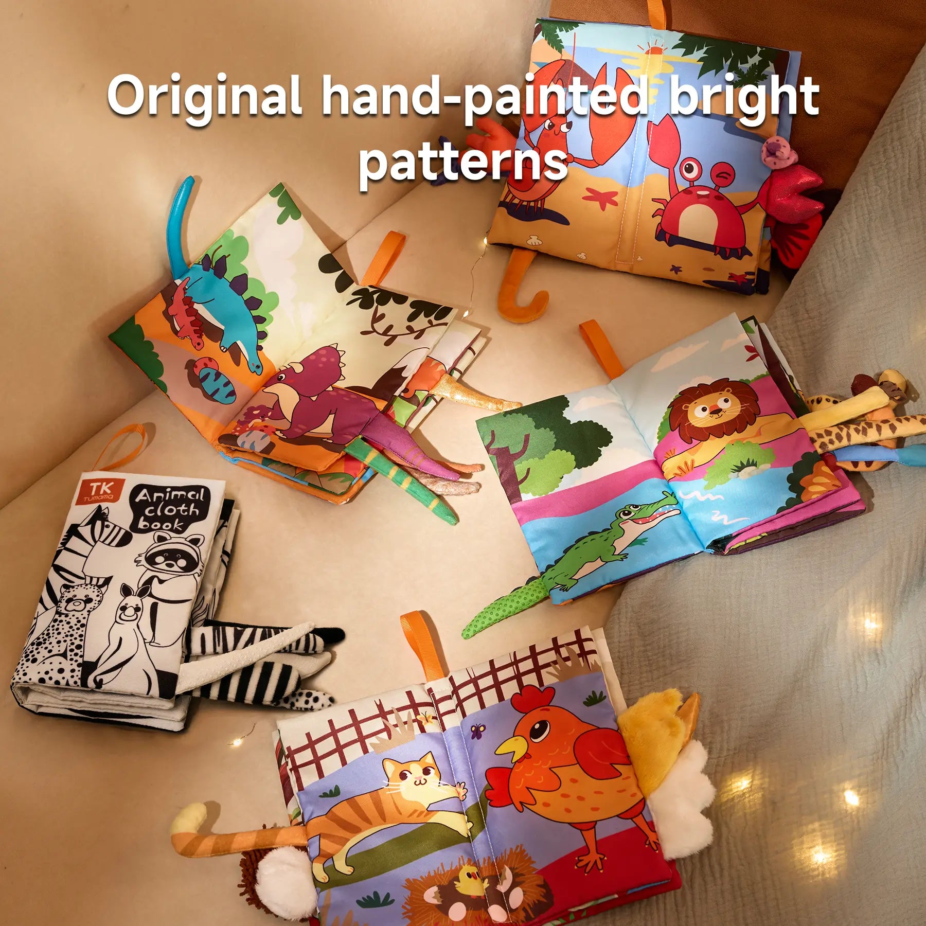 Colorful baby cloth books laid open to reveal original hand-painted animal illustrations and textured tails. Themes include dinosaurs, sea creatures, jungle animals, farm animals, and black-and-white high-contrast animals. Each book features bright, eye-catching patterns and soft fabric tails.