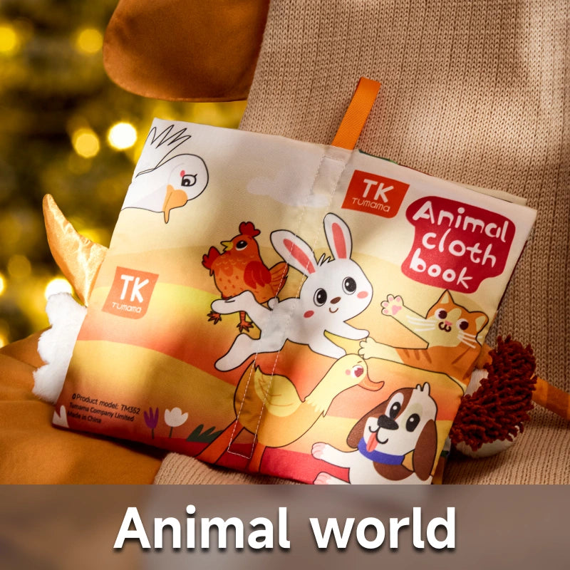 Bright and cheerful Animal Cloth Baby Book from TK Tumama, shown resting on a soft beige chair with festive warm lighting in the background. The cover features cute cartoon animals including a rabbit, cat, dog, duck, and bird. Several plush animal tails extend from the book’s edge. Text at the bottom reads: “Animal world,” emphasizing the farm and pet animal theme designed for early sensory and visual development.
