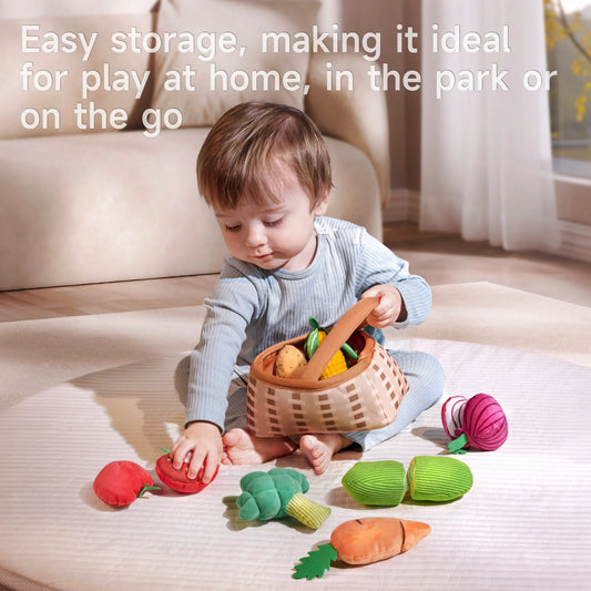 baby plays with a basket of felted vegetable toys in a cozy indoor setting. The basket overflows with colorful toys—a red tomato, an orange carrot, a white onion, and green broccoli.