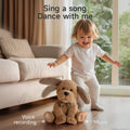 A toddler in white clothes stands behind an interactive plush dog toy with floppy ears on the living room floor, showing the toy’s voice recording and music features.