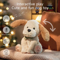 Interactive stuffed animal dog toy with beige fur and floppy brown ears, sitting on a knitted cushion in a cozy room with warm lighting and a decorated Christmas tree in the background. Arrows and icons highlight its features: music playback, voice recording, ear flapping, and body shaking. Text reads 'Interactive play, Cute and fun dog toy'.