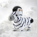 Plush zebra toy standing on fluffy, cloud-like white fabric, emphasizing its soft, realistic-looking fur. The background is filled with soft cotton clouds, and overlaid text reads 'Soft fabric for greater realism.