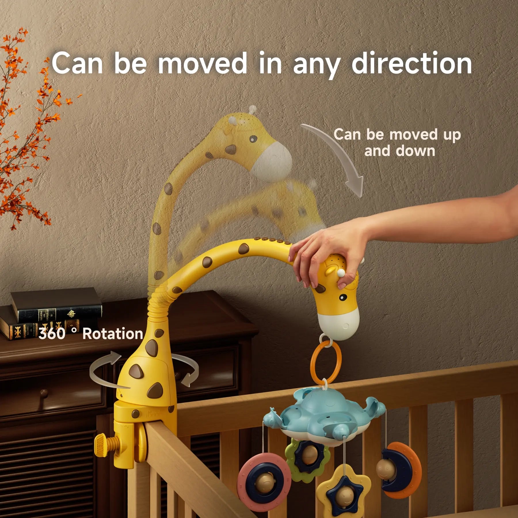 A hand adjusts a yellow giraffe-shaped crib mobile attached to the side of a wooden crib. The mobile features colorful hanging toys shaped like stars and moons. The image shows that the giraffe neck can move up and down and rotate 360 degrees for flexible positioning. White overlay text reads “Can be moved in any direction,” “Can be moved up and down,” and “360° Rotation.”
