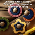 Close-up of four colorful baby crib mobile toys placed on a brown fabric background. The toys are shaped like flowers, stars, and moons, each with a smiling round face in the center. They are made of chewable material. White overlay text reads: “Chewable material, support 150°C (248°F) high temperature disinfection or boiling.”