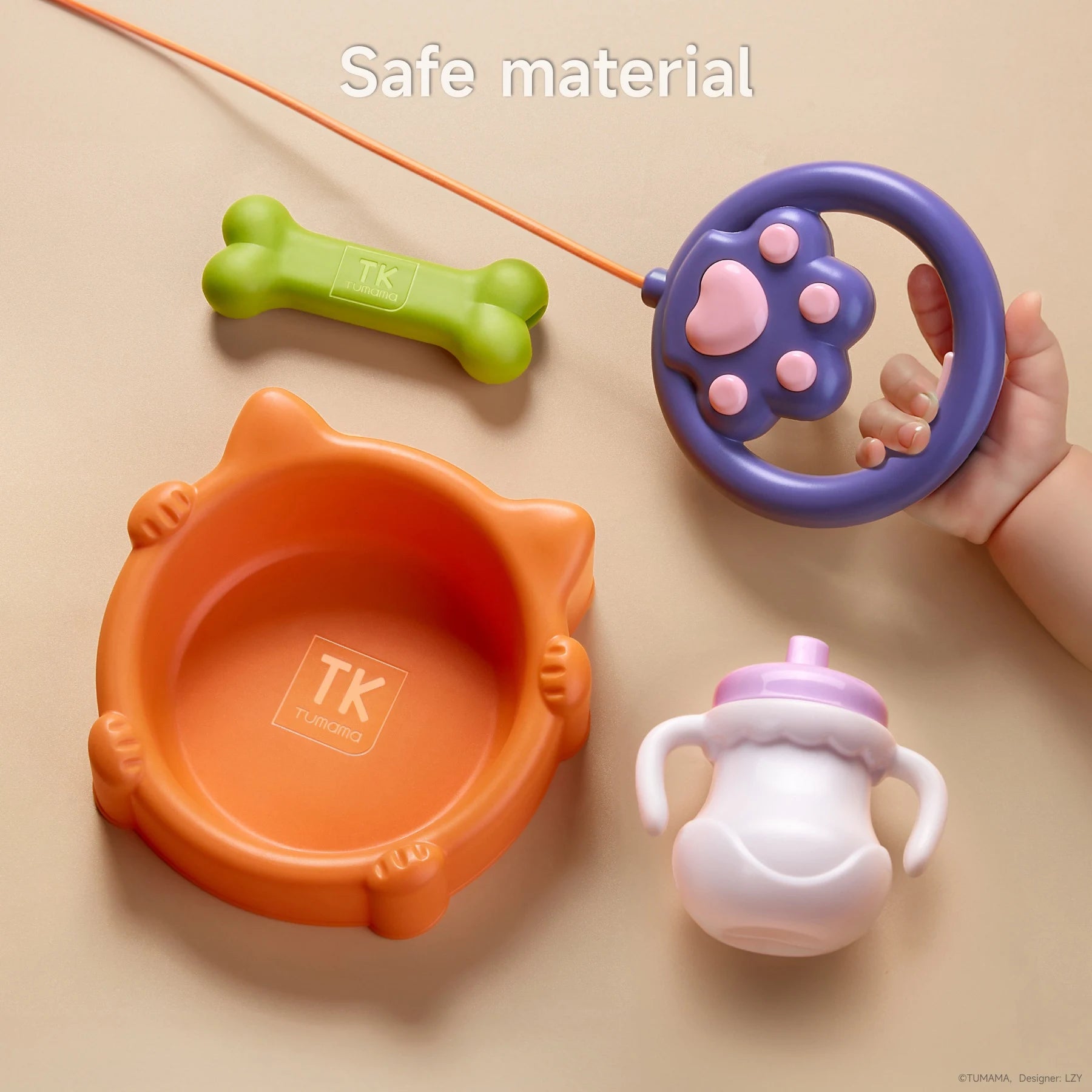 Top view of toy dog accessories made from safe materials, including an orange cat-shaped food bowl labeled 'TK Tumama', a green bone, a purple and pink paw-shaped leash handle held by a child's hand, and a white and pink sippy cup, all placed on a beige background. Caption reads: 'Safe material'.
