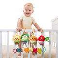 Smiling baby standing in a white crib, holding onto the railing with four colorful plush vegetable toys hanging from orange hooks. Each toy has a different design, including a sunflower, lettuce, onion, and beetroot, all with cheerful faces and textured teether shapes attached below.