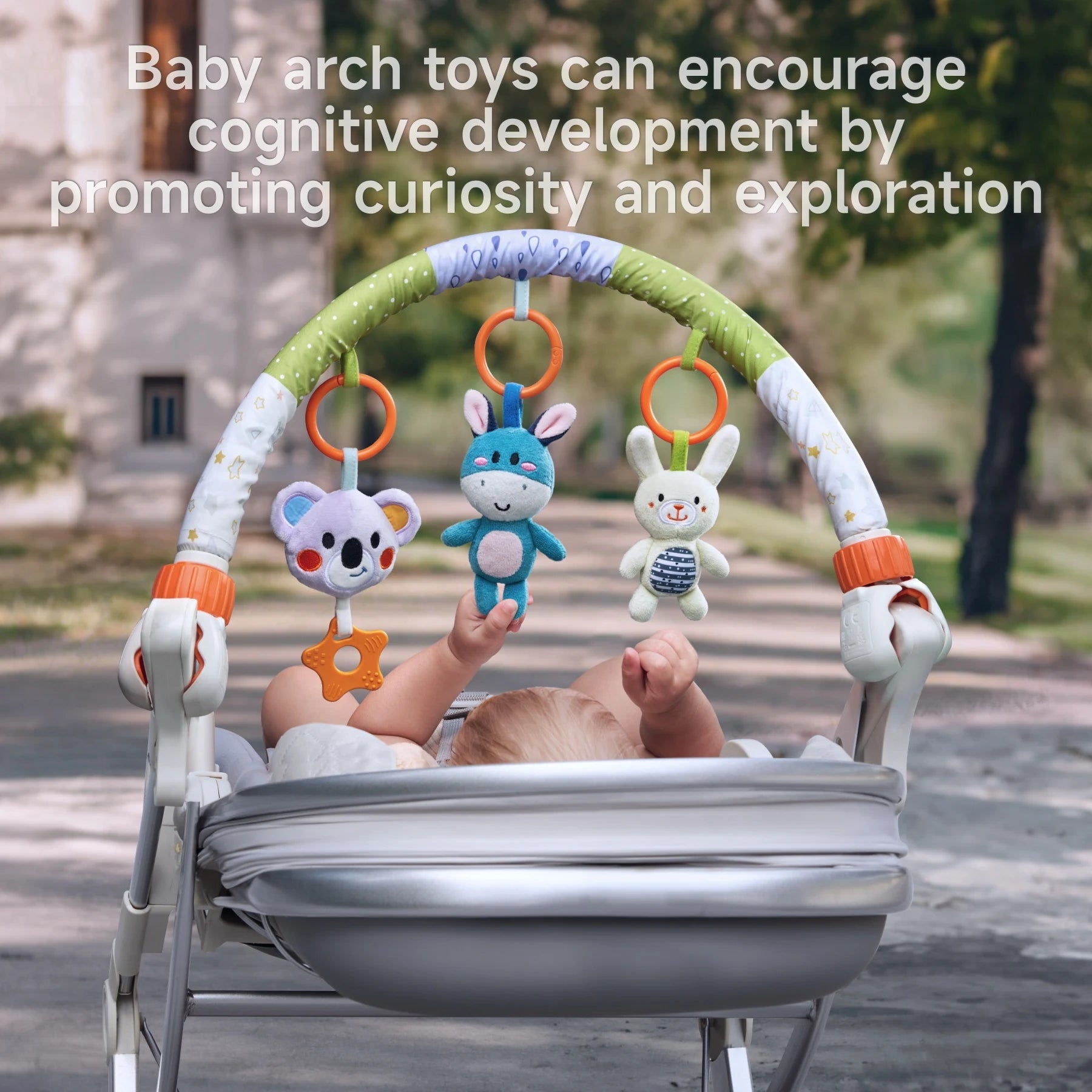Infant lying in a stroller reaching toward colorful plush animal toys hanging from a baby arch; caption highlights cognitive development benefits through curiosity and exploration.
