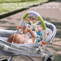 Baby lying in a stroller under a toy arch, reaching and grabbing soft animal toys hanging from the arch; caption notes stroller width ≤70cm (≤27.5 inches).