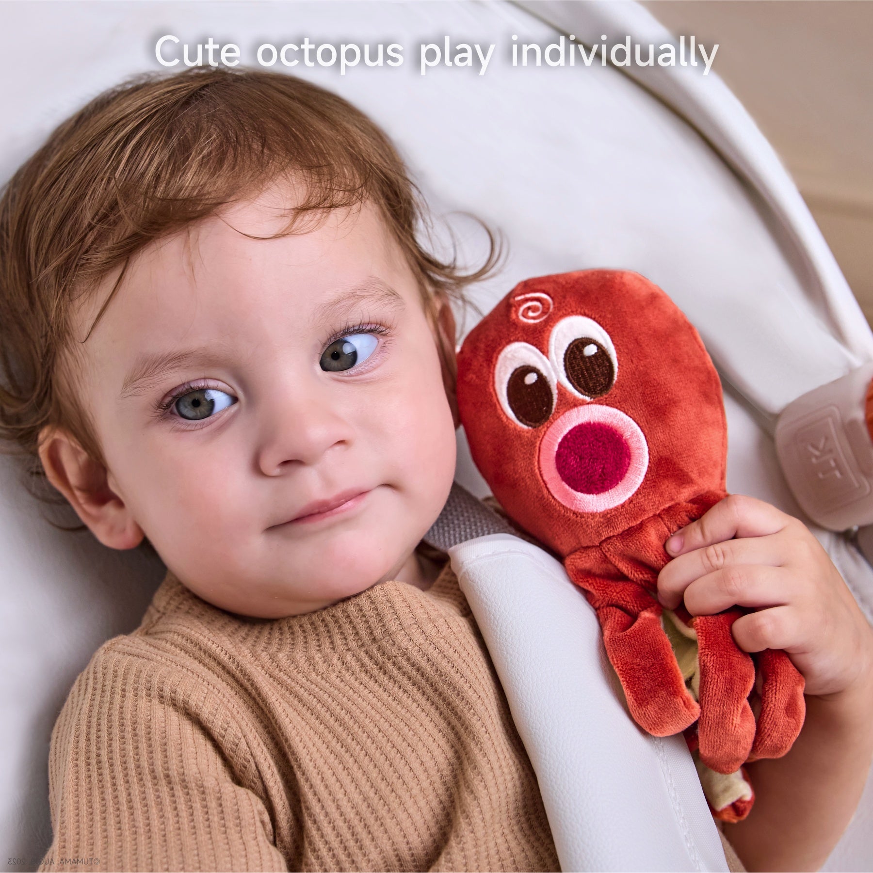 Toddler sitting in a baby seat holding a plush red octopus toy with a happy expression, showing close-up interaction with the individual toy.
