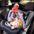 Baby sitting in a car seat playing with a colorful hanging toy bar featuring plush sea animals, including an octopus, fish, and whale.