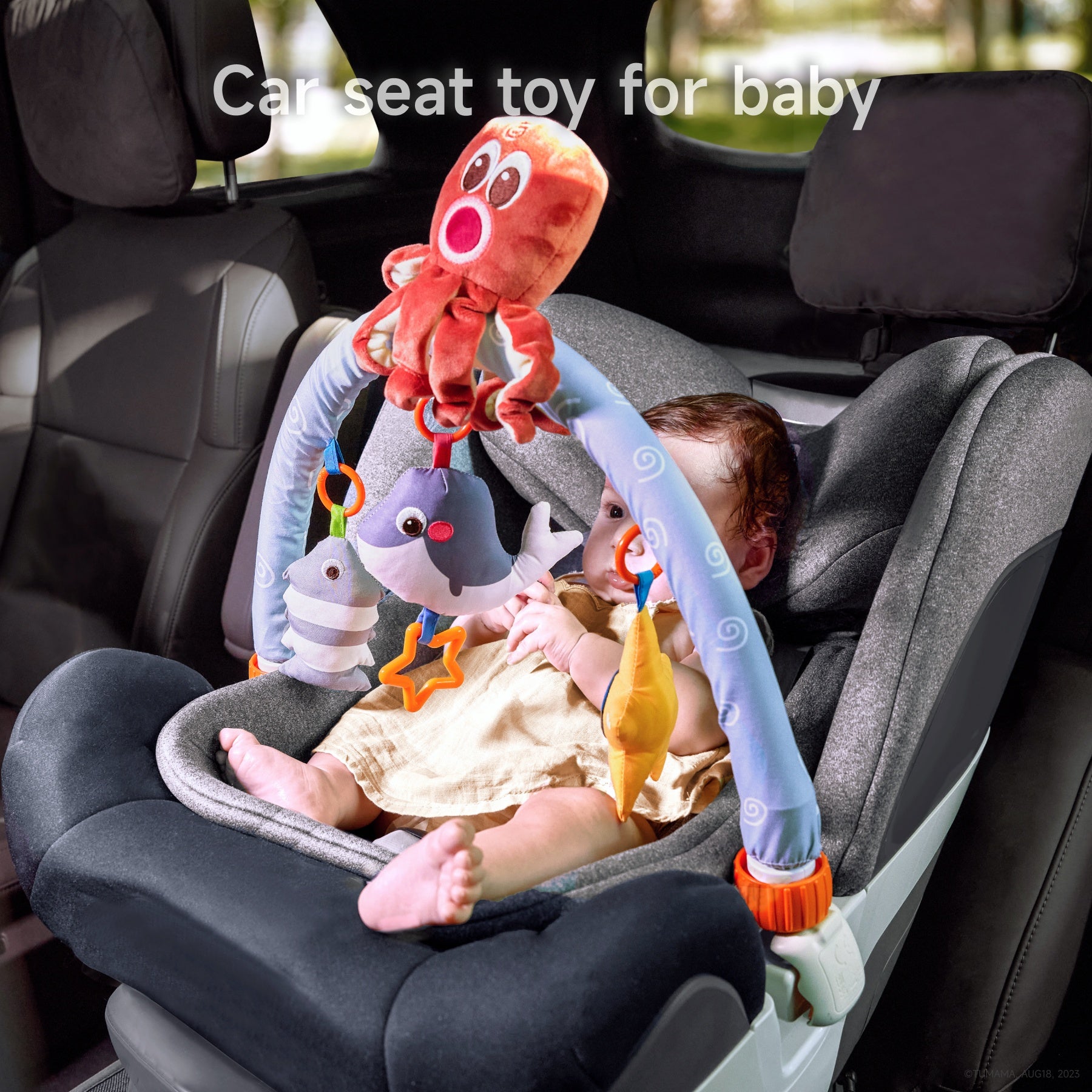 Baby sitting in a car seat playing with a colorful hanging toy bar featuring plush sea animals, including an octopus, fish, and whale.