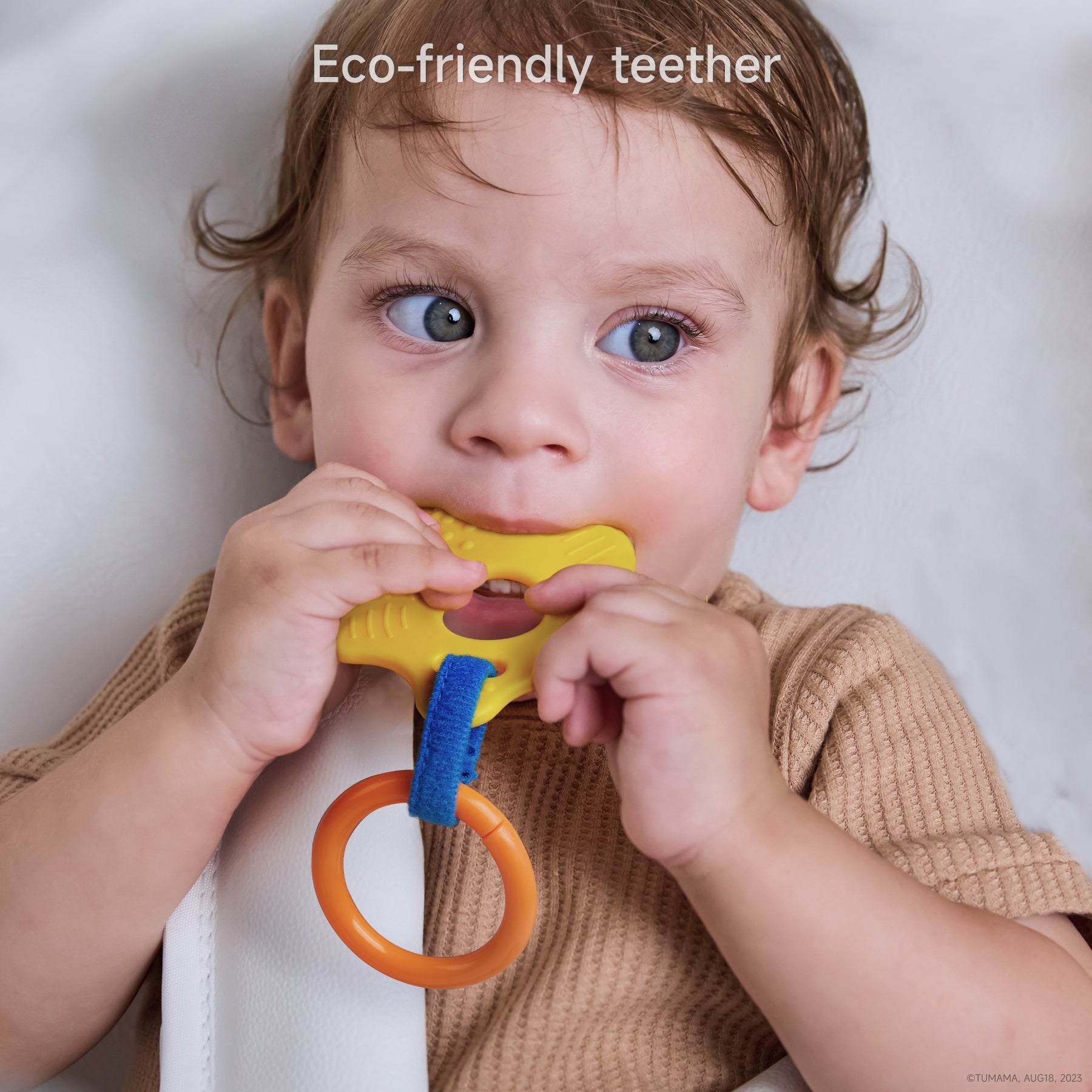 Toddler chewing on a bright yellow eco-friendly teether attached to an orange ring, wearing a brown shirt and seated in a baby chair. Caption reads: “Eco-friendly teether.”