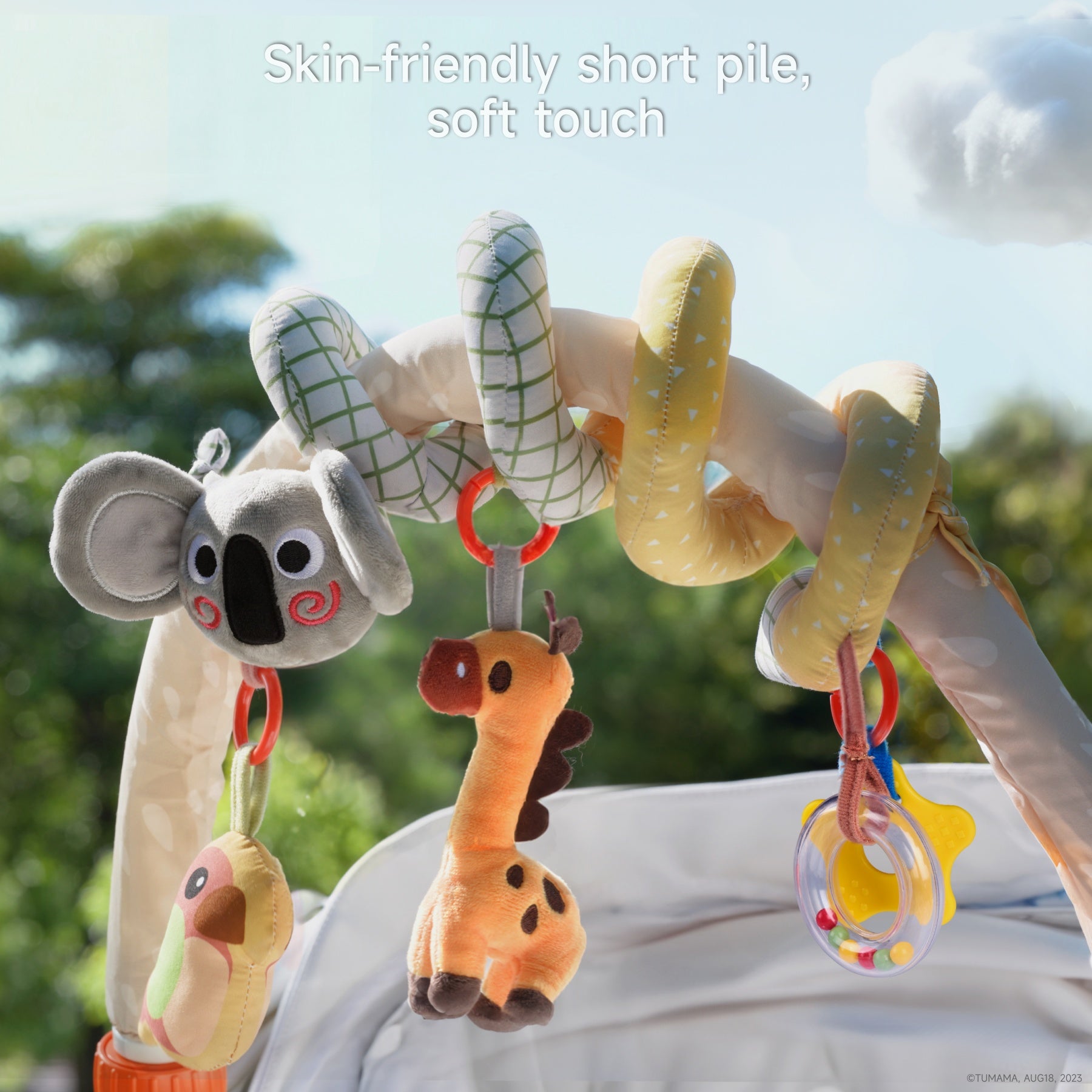 Close-up of the koala spiral arch toy attached to a stroller, featuring plush koala, giraffe, parrot, and rattle accessories. The arch has soft yellow and green fabric with a spiral design. Caption reads: “Skin-friendly short pile, soft touch.”