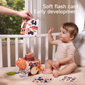 Baby sitting in crib looking at soft animal flash card for early development, with sensory tissue box toy and learning cards for visual stimulation