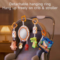 A baby stroller displays a detachable hanging toy set featuring colorful plush animals, a mirror, soft rattles, and fabric books. The toys are suspended from orange rings on a curved handle, showcasing how the set can be easily attached to strollers or cribs.