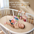 A baby lies in a white crib holding a colorful soft cloth book with animal illustrations. Along the crib rail, detachable plush toys including a crocodile, hedgehog, rabbit, octopus, and a baby-safe mirror are clipped on. Text on the image highlights the toy set's adorable design, cute patterns, and bright color combination.