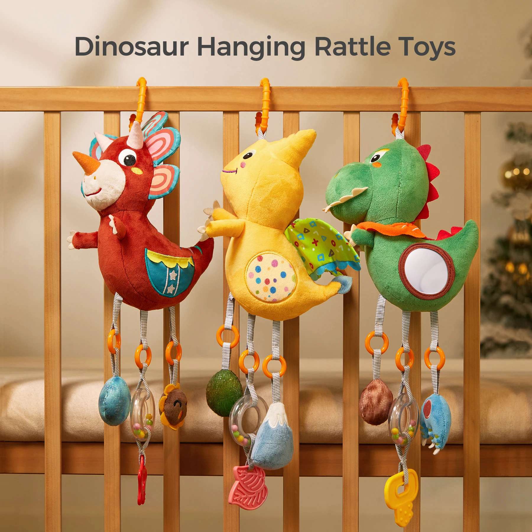 Three colorful dinosaur-themed hanging rattle toys (a red triceratops, a yellow pterodactyl, and a green T-Rex) are attached to a wooden crib rail. Each plush toy features dangling sensory accessories including a mirror, teether, rattle, and textured toys, designed to stimulate a baby’s visual, auditory, and tactile senses.