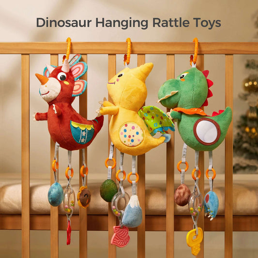 Three colorful dinosaur-themed hanging rattle toys (a red triceratops, a yellow pterodactyl, and a green T-Rex) are attached to a wooden crib rail. Each plush toy features dangling sensory accessories including a mirror, teether, rattle, and textured toys, designed to stimulate a baby’s visual, auditory, and tactile senses.
