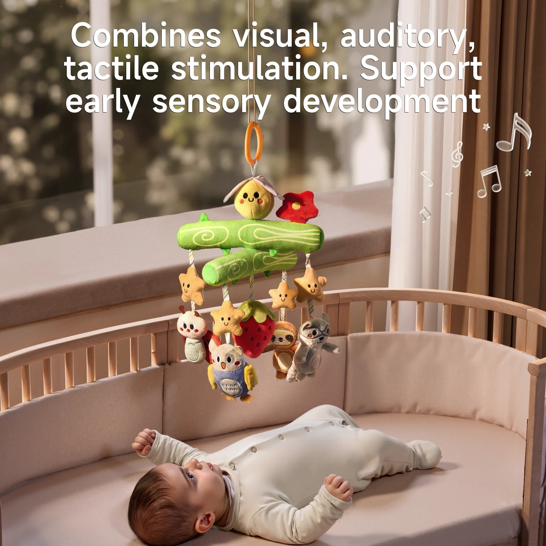 A baby lying in a crib looks up at a Woodland Animal Crib Mobile hanging above. The mobile features a green tree branch design with a plush bee and red flower on top, and hanging plush toys including stars, a ladybug, an owl, a strawberry, a sloth, and a raccoon. Musical notes are illustrated around the mobile, and text on the image reads, "Combines visual, auditory, tactile stimulation. Support early sensory development." The scene is softly lit with a cozy, natural background.
