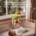 A baby lying in a crib looks up at a Woodland Animal Crib Mobile hanging above. The mobile features a green tree branch design with a plush bee and red flower on top, and hanging plush toys including stars, a ladybug, an owl, a strawberry, a sloth, and a raccoon. Musical notes are illustrated around the mobile, and text on the image reads, 